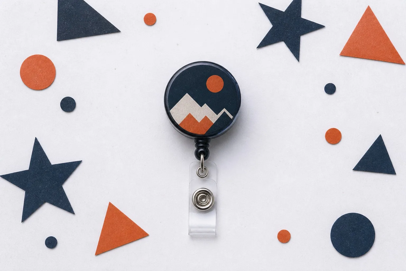 Flat-lay overhead — badge reel keychain surrounded by geometric paper shapes confetti