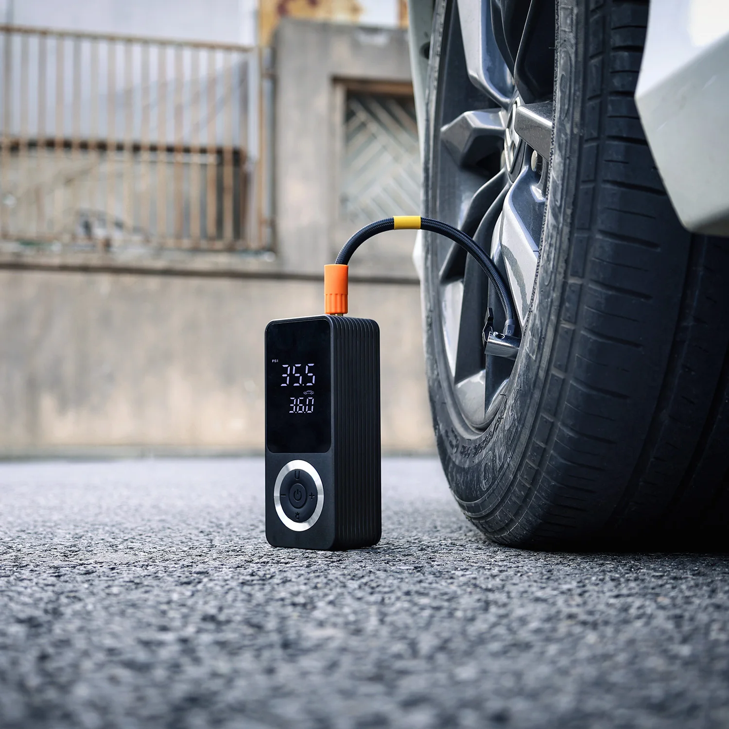 Compact cordless tire inflator placed on urban road surface next to a car wheel, ready for use