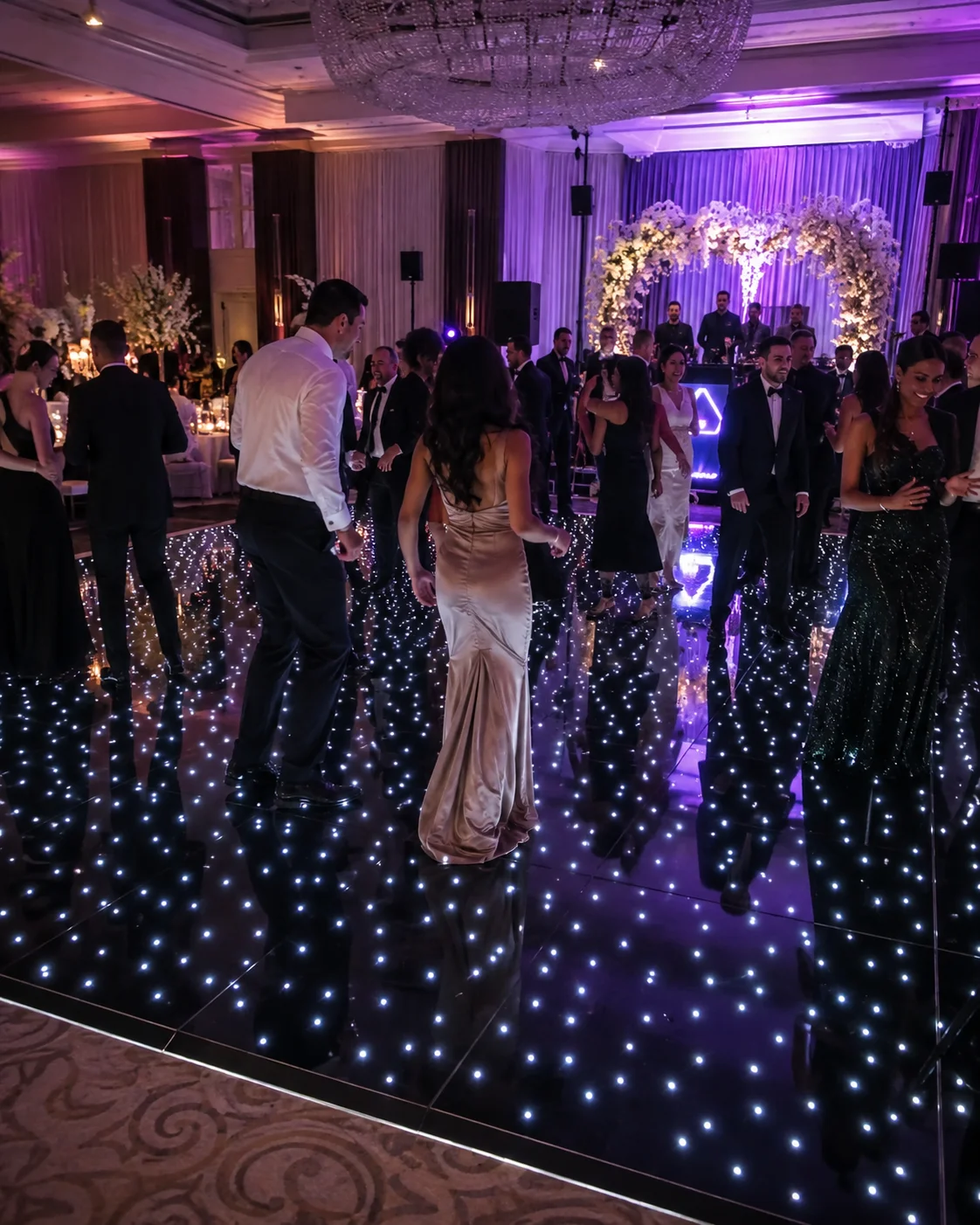 Guests dancing on a star LED dance floor at a wedding reception with colored lighting
