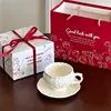 Taza de café y plato con cuchara, diseño floral color crema, con bolsa de regalo.