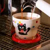 A red cat holding a coffee cup and saucer.