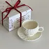 Taza de café con flor color crema y plato con cuchara.