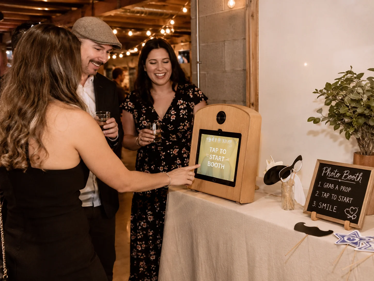 Guests using an iPad photo booth at a small indoor party with a compact wood enclosure