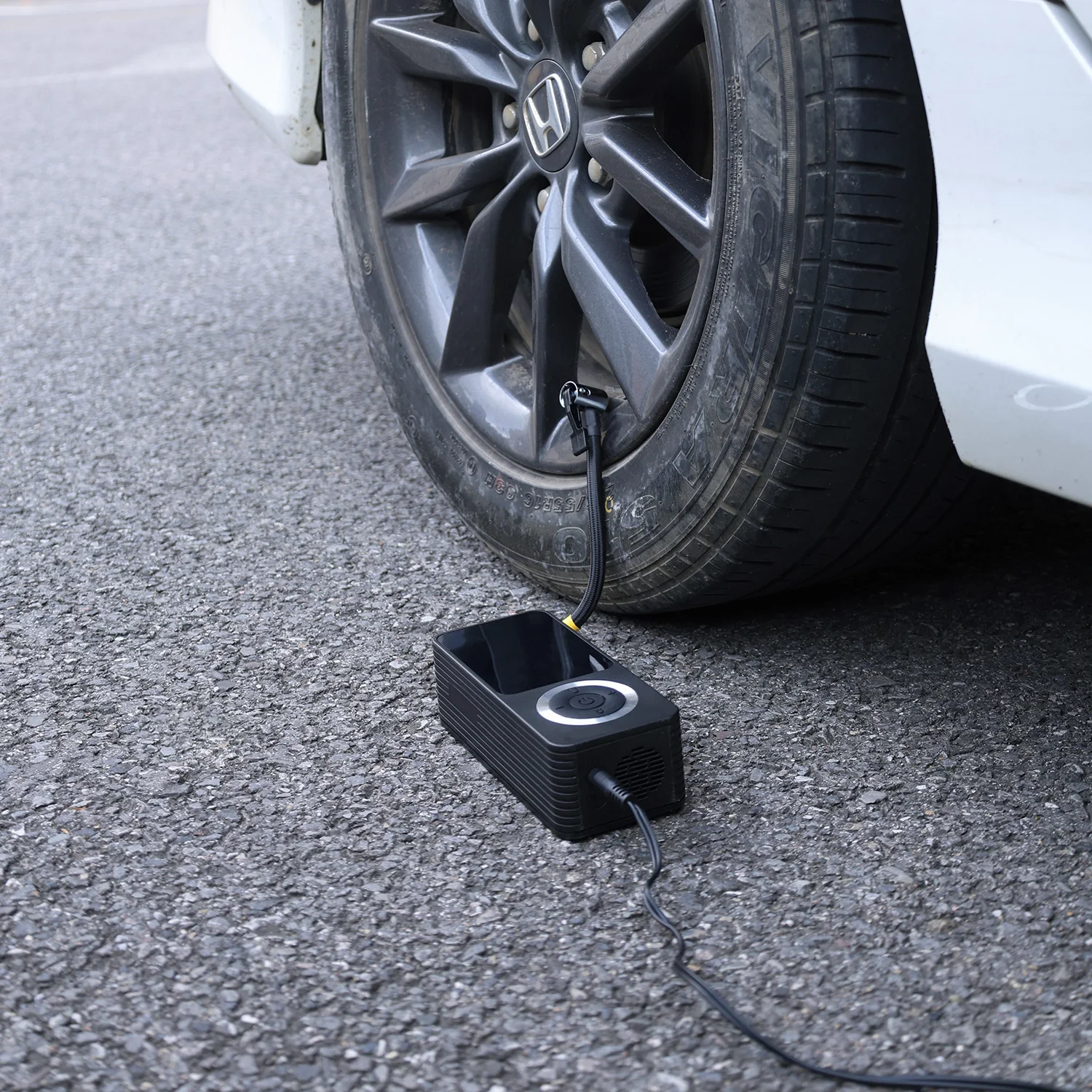Portable tire inflator connected via 12V car outlet cable to a tire on a road, showing dual power capability