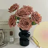 7 rosas, de color marrón oscuro, en un jarrón de cristal negro.