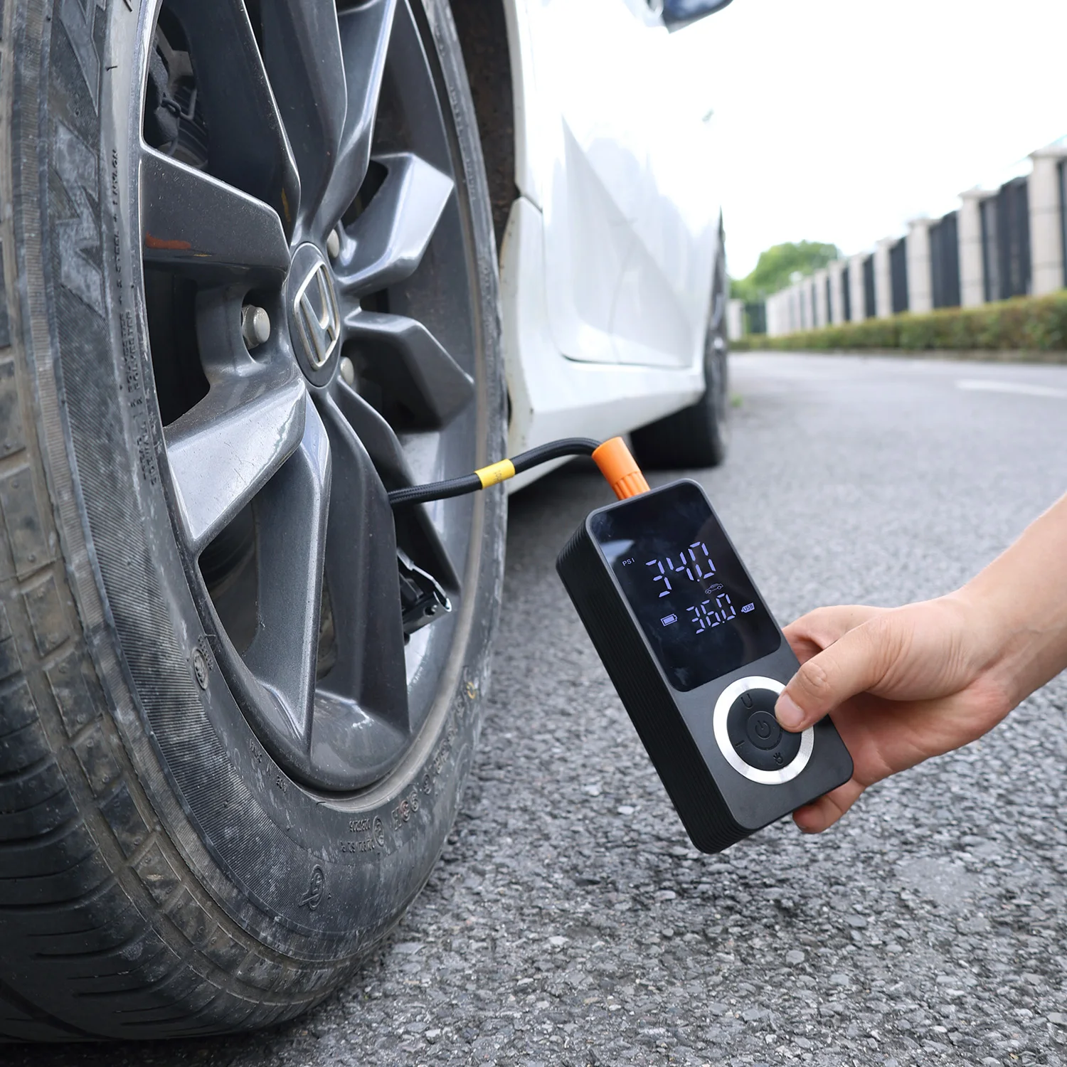 Driver kneeling beside a car tire on a road, checking tire pressure with a portable inflator