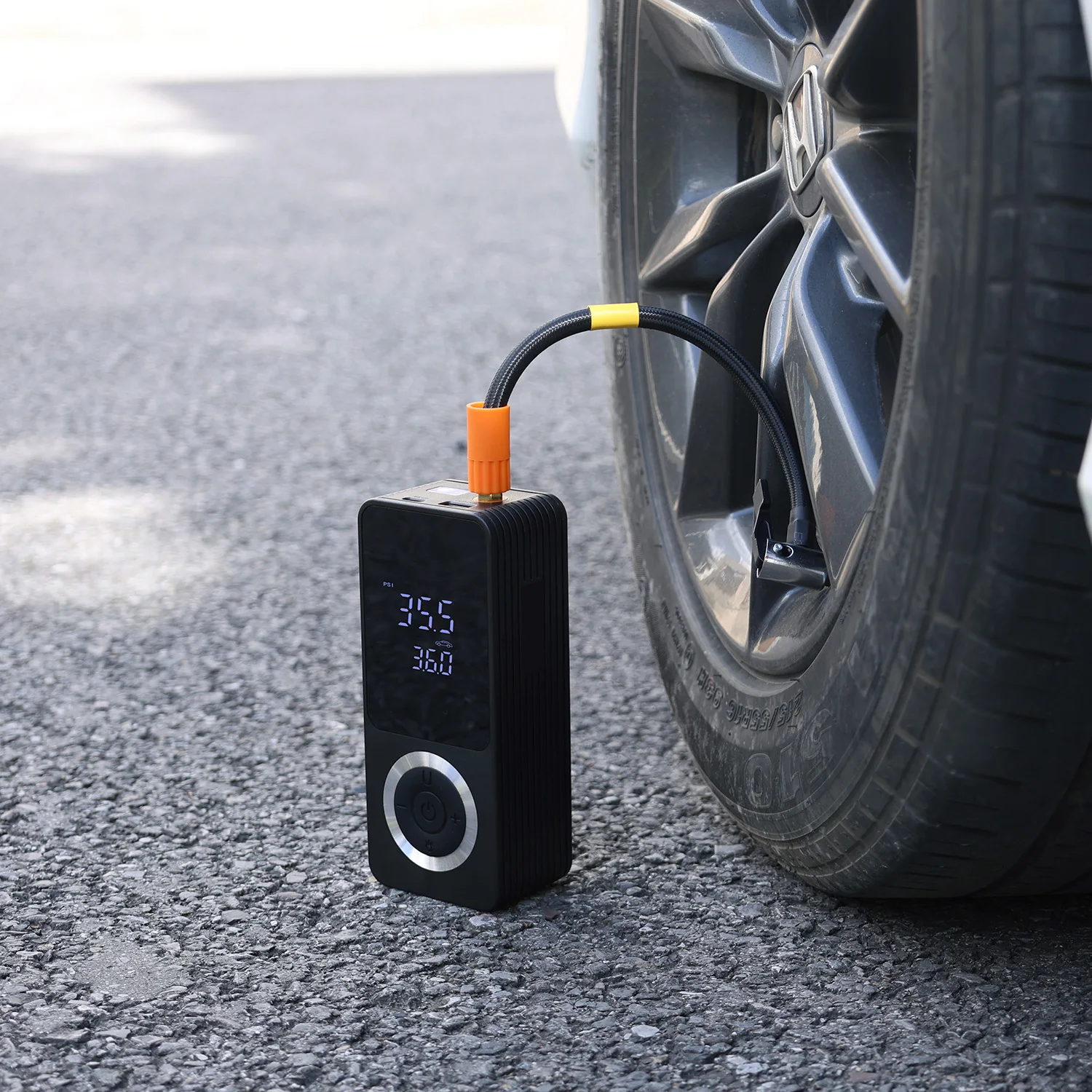Car tire on asphalt with a portable tire inflator connected to the valve stem, digital display visible