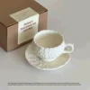 Taza de café con flor color crema y plato.