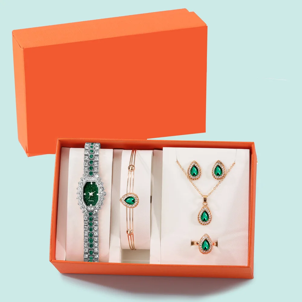 Elegantses oranžis kinkekarbis naistele mõeldud kinkekomplekt, mis sisaldab roheliste kividega hõbedast käekella, käevõru, kõrvarõngaid, kaelakeed ja sõrmust valgel taustal.