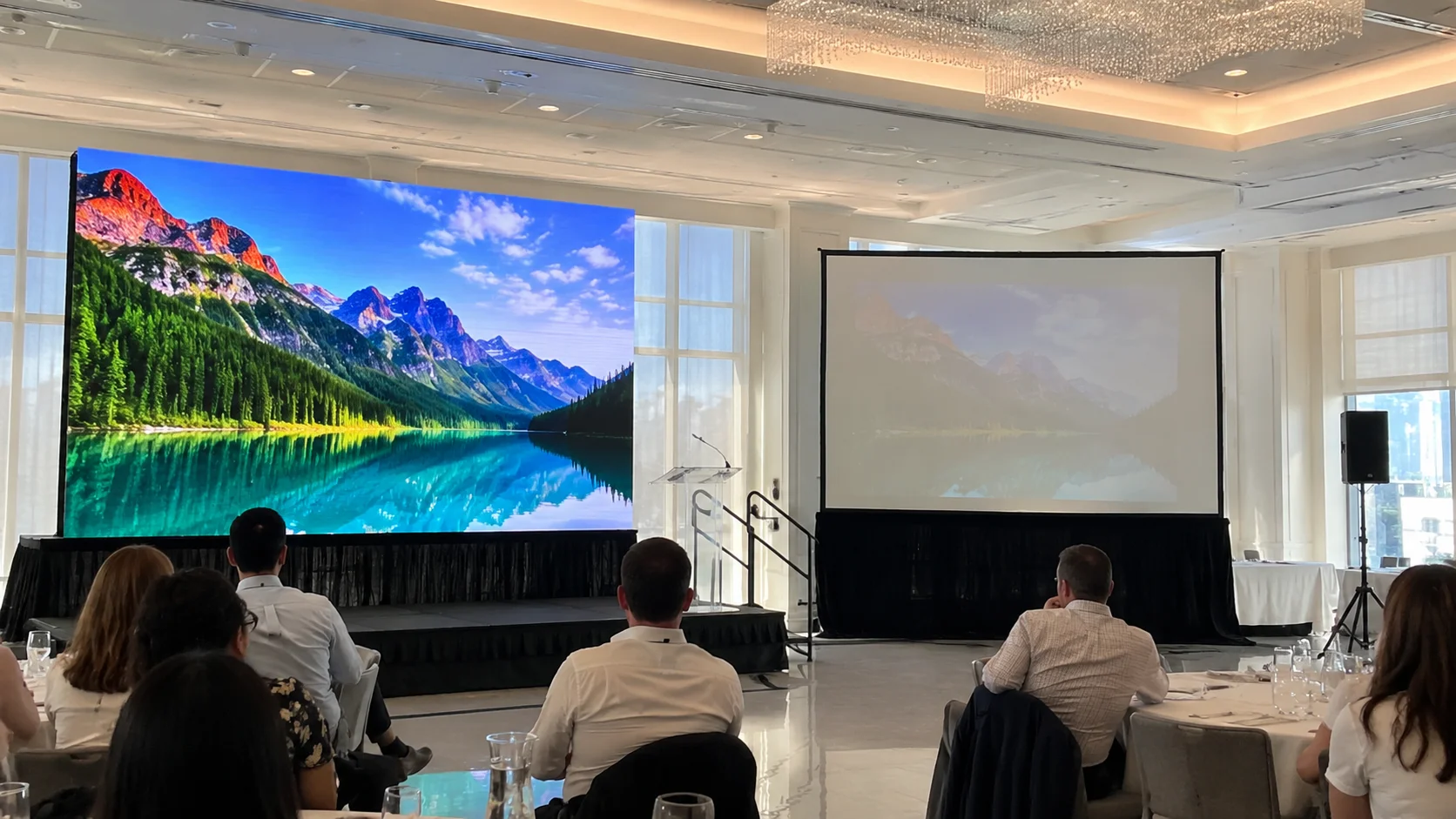 Side-by-side comparison of an LED video wall and a projector screen in a bright event hall